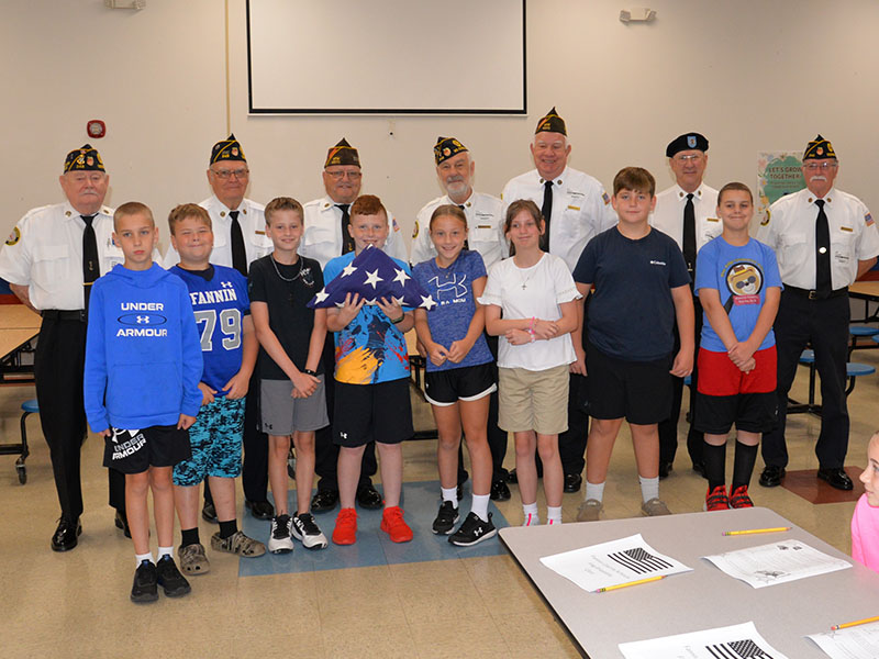Blue Ridge Elementary School fifth grade students from left, front, Justin Burrell, Mason Patterson, Aiden Owensby, Zeke Payne, Alexandria Evans, Annabelle Rainwater, Cason Dyer, and Troy Taylor display the American flag that they just practiced folding as veterans Chief “Mac” McMillen, Chris McKee, Richard Crosley, Steve Strickland, Jim Wallace, Bob Herrington, and Bill Stodghill stand behind them. 