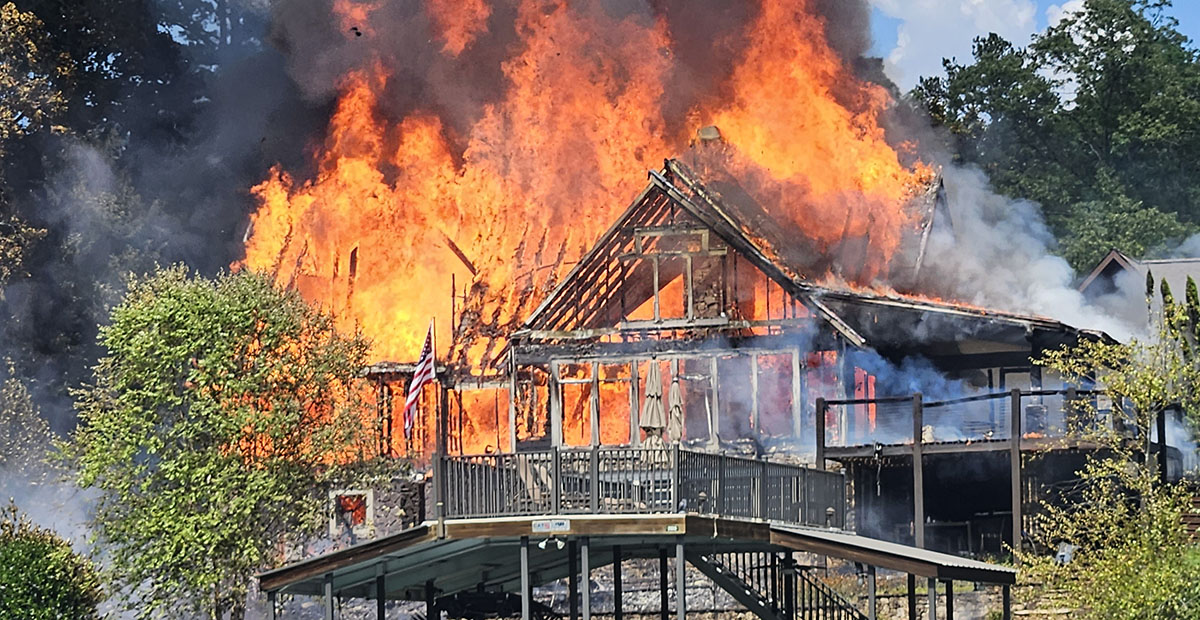 This photo of a fire at a Blue Ridge Lake home was believed to have been taken only minutes after firefighters were called to the scene shortly before 3 p.m. last Wednesday, July 26. The resident who was at home reported discovering the blaze when the entire front of the structure, facing the lake, was already fully involved in flames. Neighbors removed the boat shown in the foreground to a different dock.