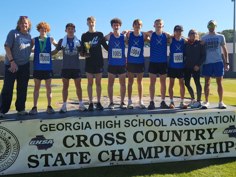 Shown on the podium celebrating their fourth place finish in the Cross Country State Championships are, from left, coach Suzianne Pass, Koen Verner, Zechariah Prater, Luke Callihan, Conner Kyle, Rylin Davis, Gage Bryan, Mason Sandefer, coach Miranda Roof, and coach Lucas Roof.