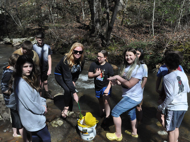 Students, left, Isabella Davenport, Tori Arp (STEM Teacher), Olivia Harris, Molly Howard, and Rivers Halpin were having so much fun releasing their trout into the stream.