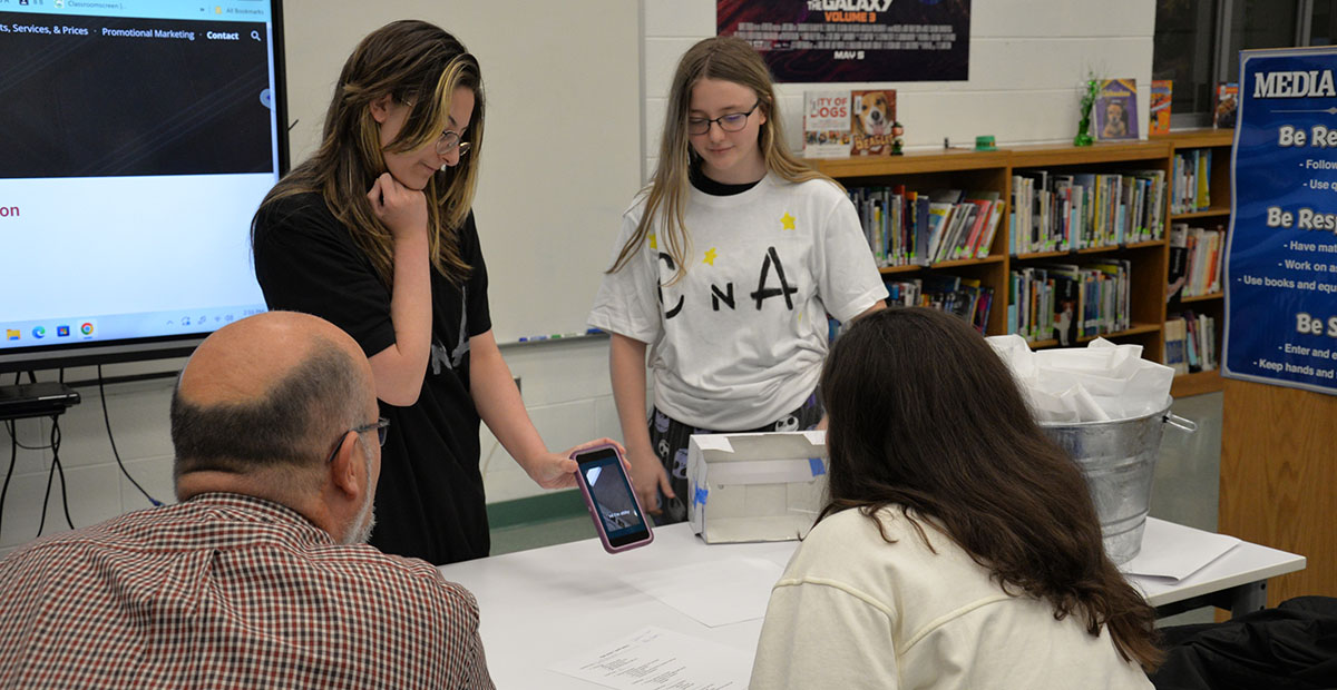 First place winners of Fannin County Middle School’s Shark Tank, Caroline Cole, left, and Abby Pickard show Erick Youngberg and Christie Gribble the commercial for their holographic movie theater business.