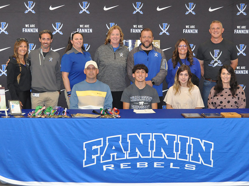 Proud coaches and volunteers pose with Zechariah Prater, seated with his family, when he signed his Letter of Intent to run track and field at Charleston Southern University. Shown from left are Head Coach Miranda Roof, volunteer coach Dr. Lucas Roof, Hannah Godfrey, Suzianne Pass, Principal Scott Ramsey, Athletic Director Shannon York, and volunteer coach Chad Galloway. 