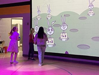 West Fannin Elementary School students are now able to continue learning new academic lessons outside of the classroom thanks to the gym’s new Lu Interactive Playground. Students are shown, above, excitedly answering math problems in a gym that has been transformed with technicolor lights and an interactive screen.
