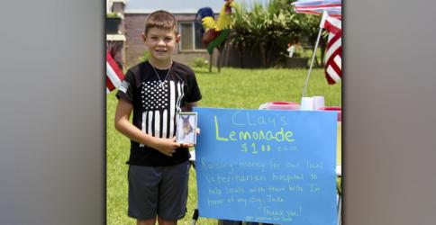Clay Maddox, age 9, of Morganton, stands next to his lemonade stand in front of his home off Morganton Highway, where he is raising funds for Ocoee Animal Hospital in honor of his recently passed German Shepherd, Jake, pictured in the frame.