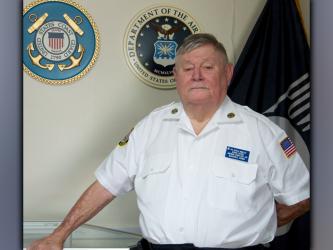 Retired United States Coast Guard veteran Gerald “Chief Mac” McMillen stands before the U.S. Coast Guard emblem at the Fannin County Veterans Museum.