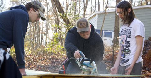Fannin County High School students Trey Combs, Brandon Rhodes and Paul McCormick, from left, work together to saw a piece of plywood for the latest Habitat for Humanity of Fannin & Gilmer Counties build Friday, December 3.