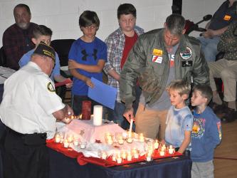West Fannin Elementary School students, from left, Bently Cole, Colton Dills and Jonah Strobel watch as Joey Gryzenia, a member of the US Coast Guard, participates in the candle lighting ceremony at their Veteran’s Day Progam. To his right are his sons Maddox Gryzenia and Miller Gryzenia who are also students at West Fannin.
