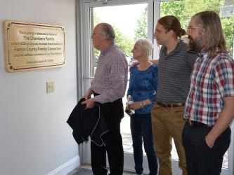 Glenn Chambers reads the plaque on the wall at the entrance to Fannin County Family Connection recognizing his family for their donation of the building. He is joined by his wife, Lynda, and their sons, Chris and Patrick.