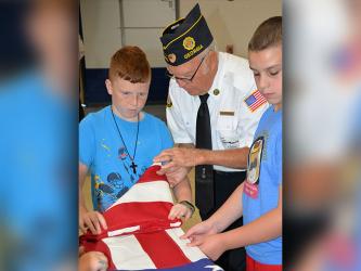 Blue Ridge Elementary School fifth grade students Zeke Payne and Troy Taylor follow instructions from veteran Chris McKee as he demonstrates how to tuck the folds of the United States flag neatly. This was part of a local program offered by area veterans organizations.